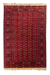 Alfombra oriental roja con patrón repetitivo de medallones geométricos y guardas tribales tradicionales.