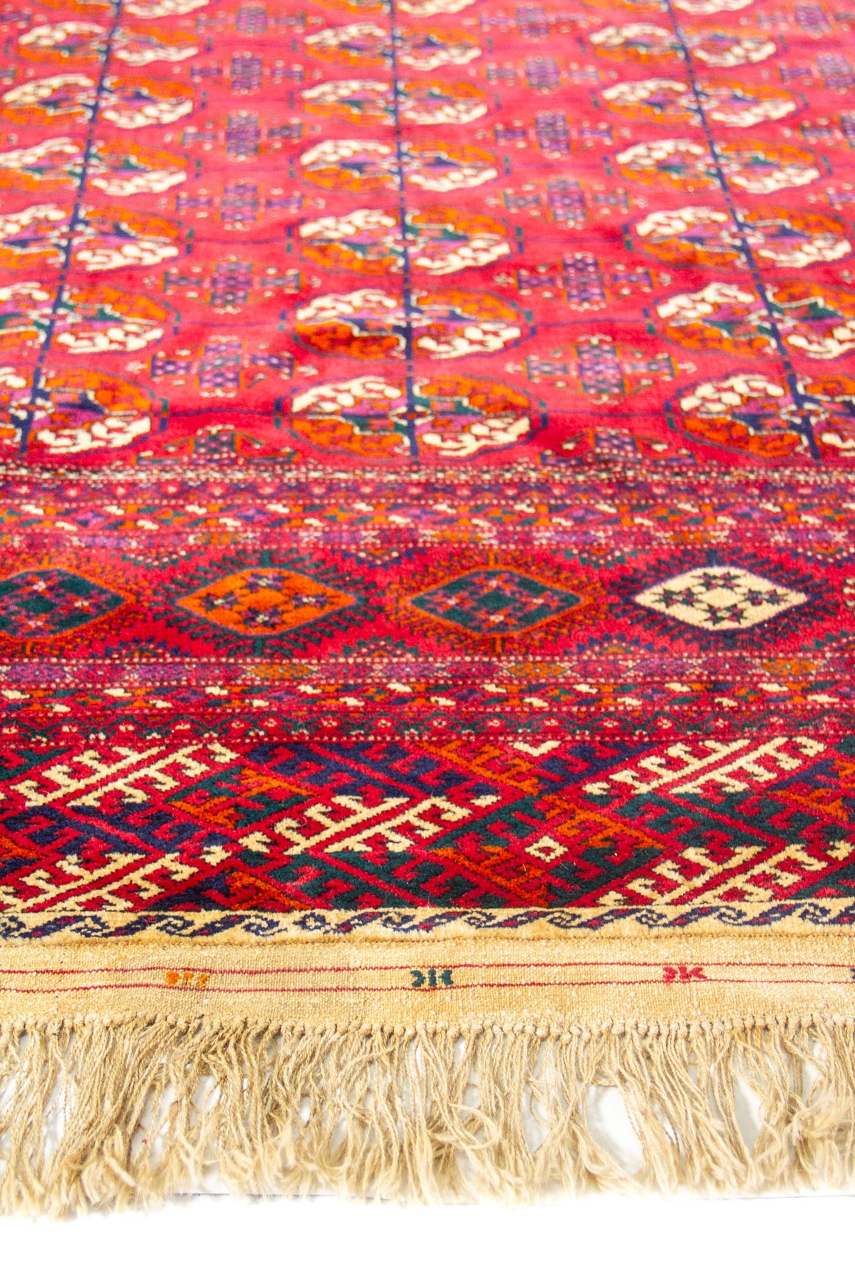 Detalle de alfombra roja con motivos geométricos repetitivos y guarda decorativa en tonos burdeos y azul marino.