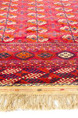Detalle de alfombra roja con motivos geométricos repetitivos y guarda decorativa en tonos burdeos y azul marino.