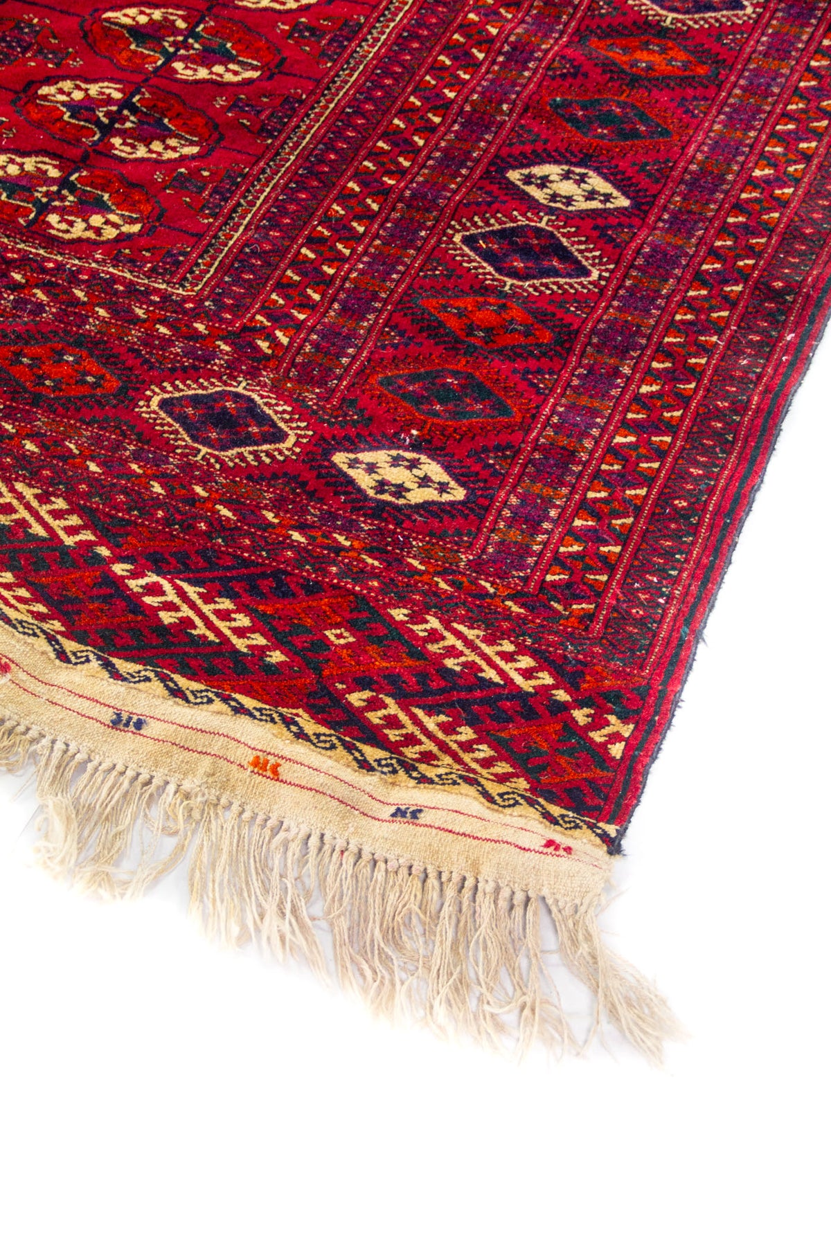 Primer plano de borde de alfombra oriental roja con diseño tribal y flecos tejidos a mano.