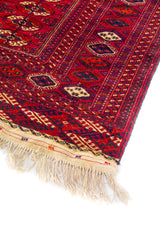 Primer plano de borde de alfombra oriental roja con diseño tribal y flecos tejidos a mano.