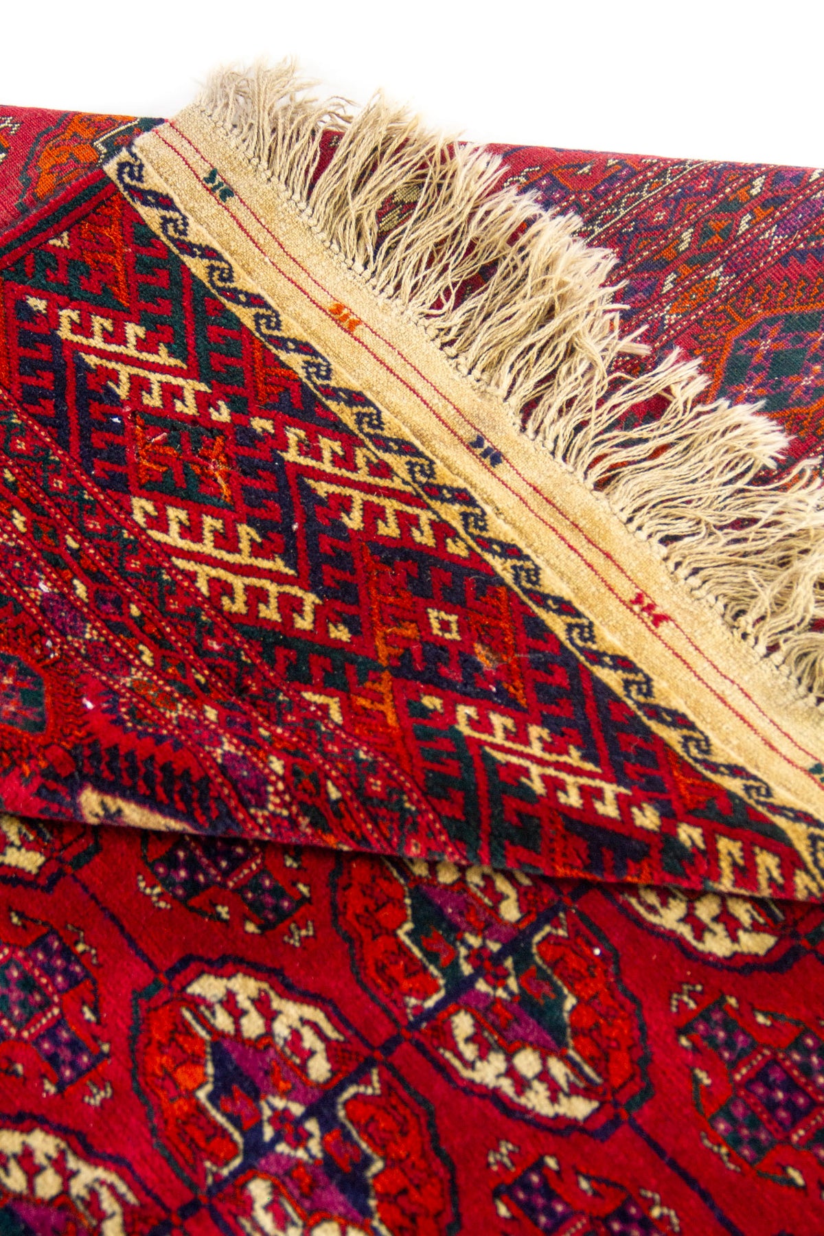 Detalle de esquina de alfombra roja con patrones geométricos tradicionales y acabado artesanal.