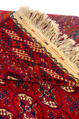 Detalle de esquina de alfombra roja con patrones geométricos tradicionales y acabado artesanal.