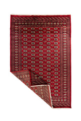 Alfombra Bokhara doblada mostrando el reverso del tejido y los flecos, destacando su elaboración artesanal.