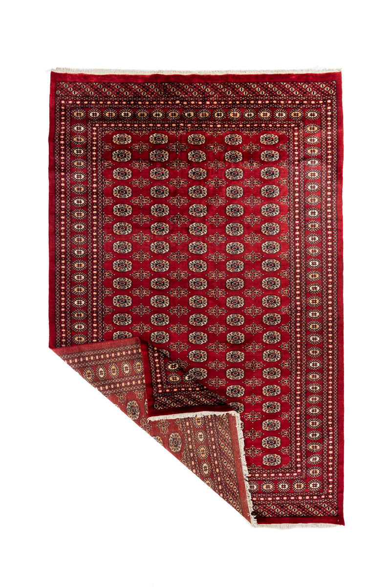 Alfombra Bokhara doblada mostrando el reverso del tejido y los flecos, destacando su elaboración artesanal.