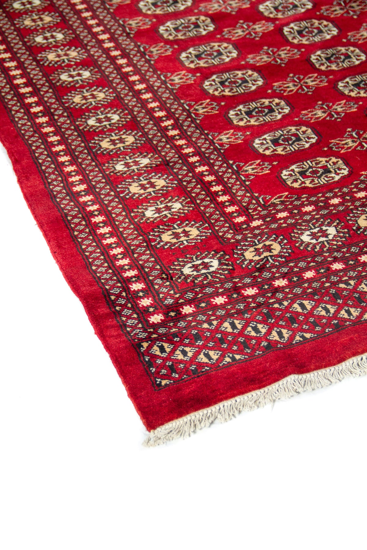 Primer plano del borde de alfombra oriental con diseño geométrico tradicional y flecos blancos.