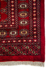 Detalle del borde y esquina de una alfombra Bokhara con patrones geométricos en tonos rojo, beige y negro.