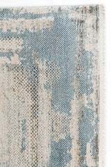 Detalle cercano del borde de la alfombra que resalta el tramado en tonos azul celeste y beige con un patrón de textura sutilmente pixelado.