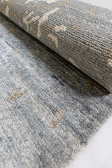 Primer plano lateral de la alfombra enrollada, destacando su textura tejida en tonos azulados y beige