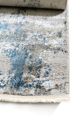 Primer plano del borde de la alfombra destacando la textura aterciopelada y los detalles azules y dorado sobre fondo claro