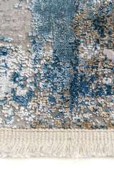 Primer plano de la textura en relieve de la alfombra con matices azul profundo, beige, dorado y blanco sobre base gris
