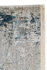 Detalle del borde de la alfombra mostrando el acabado con flecos cortos y patrón abstracto en tonos fríos
