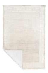 Alfombra contemporánea color marfil con una esquina doblada mostrando el reverso.