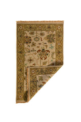 Alfombra beige con esquina doblada mostrando el reverso del tejido y el detalle de la guarda decorativa.