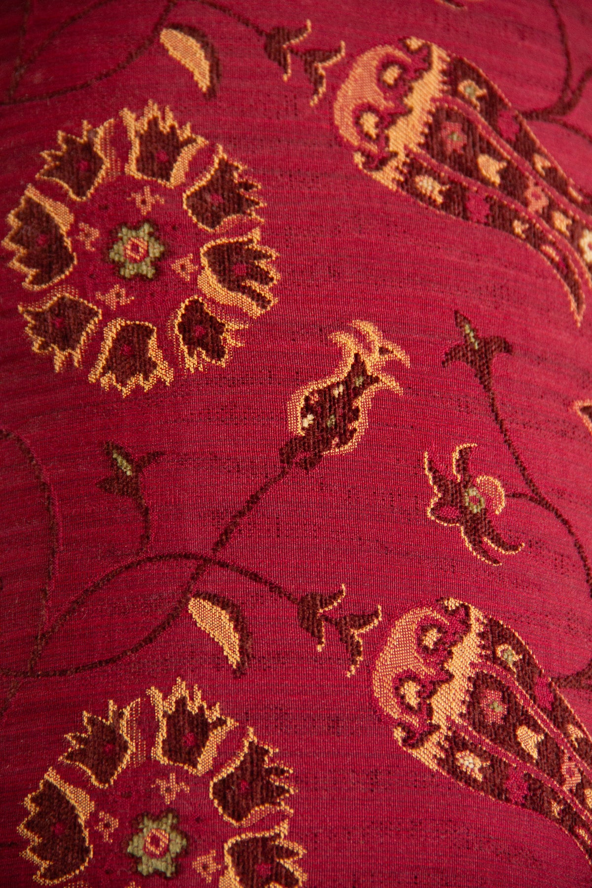 Detalle del diseño floral del almohadón bordó con hojas, flores y tonos dorados