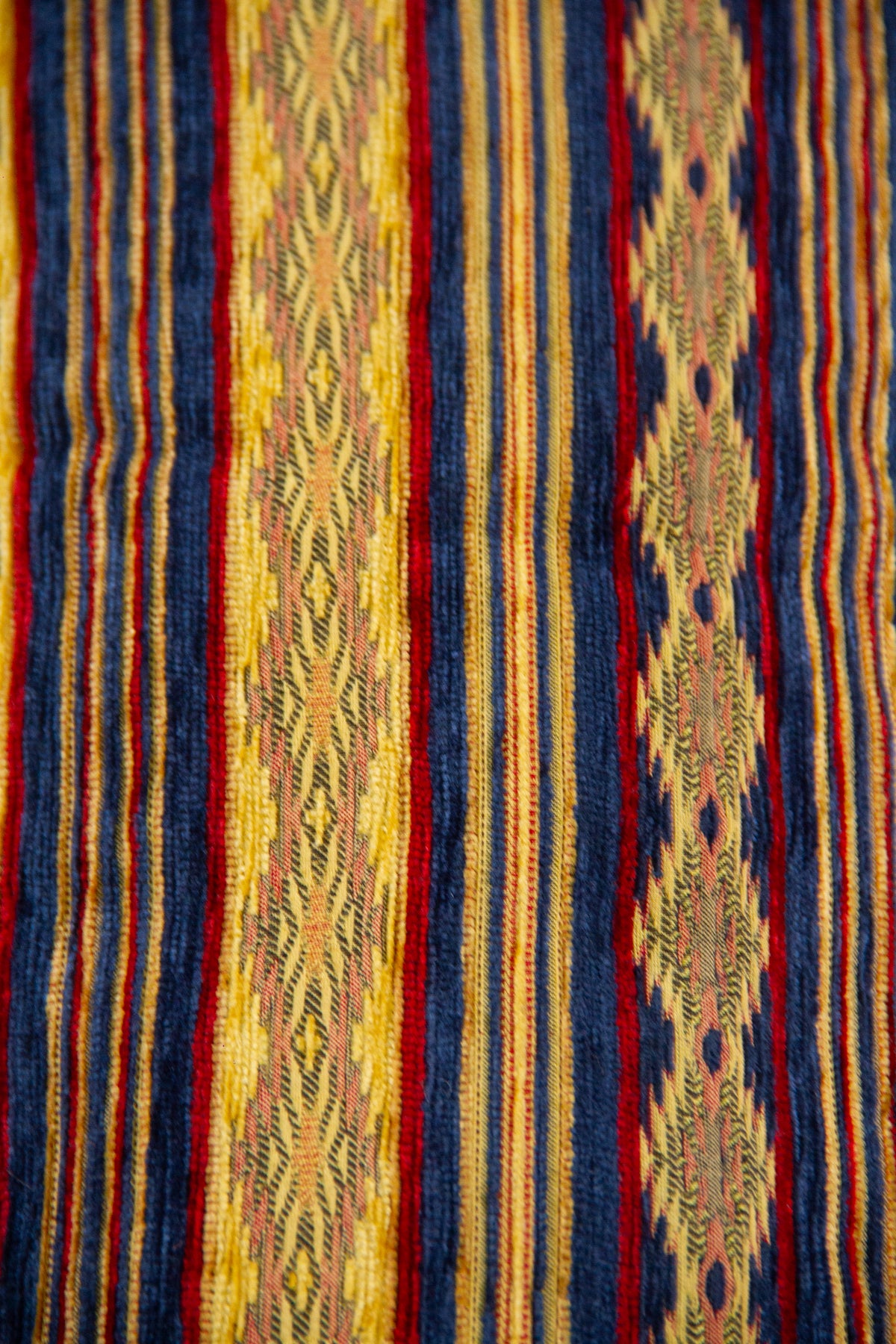 Detalle del diseño textil con rayas azules, amarillas y rojas en almohadón caramelo
