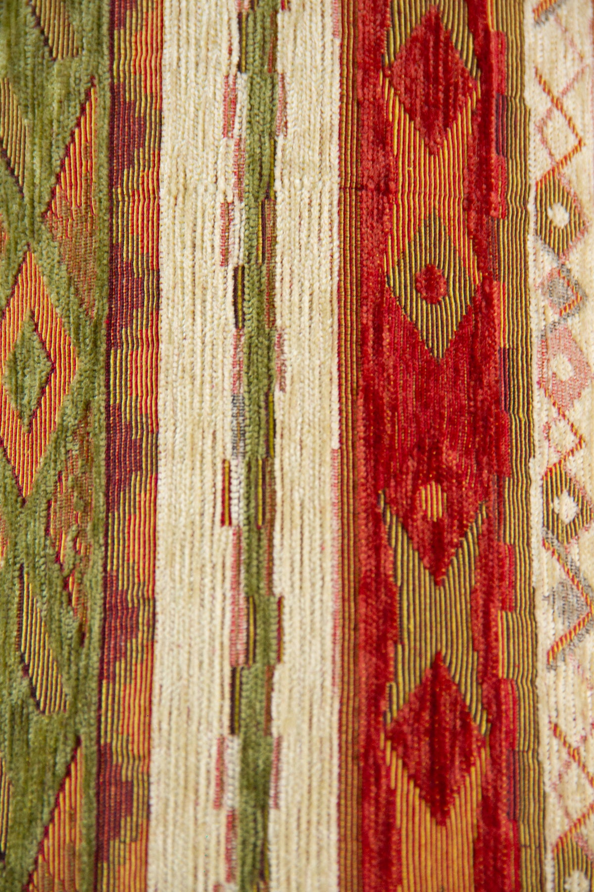 Detalle del diseño rayado y geométrico del almohadón en tonos verde, rojo y beige