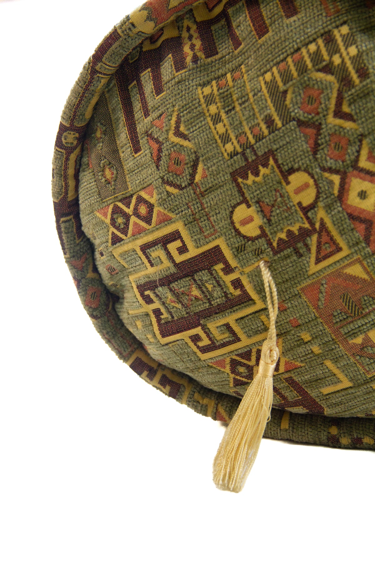 Detalle de textura de almohadón caramelo verde con motivos geométricos y borla decorativa