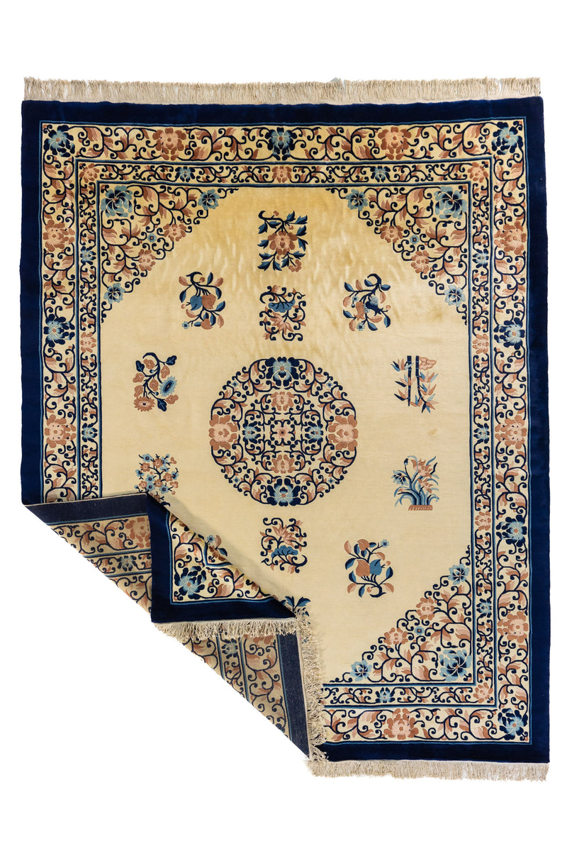 Alfombra beige y azul marino con esquina levantada, mostrando el reverso, flecos y acabado del tejido.