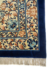 Detalle de la guarda azul marino con flores en tonos celeste y marrón, más flecos beige en el borde.