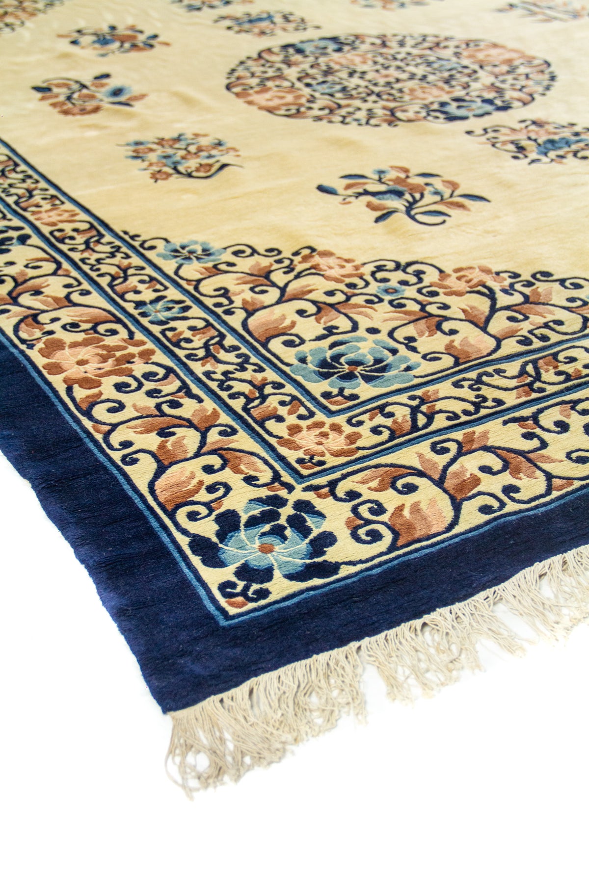 Vista en perspectiva de la alfombra beige con borde azul marino y marco floral ornamentado.