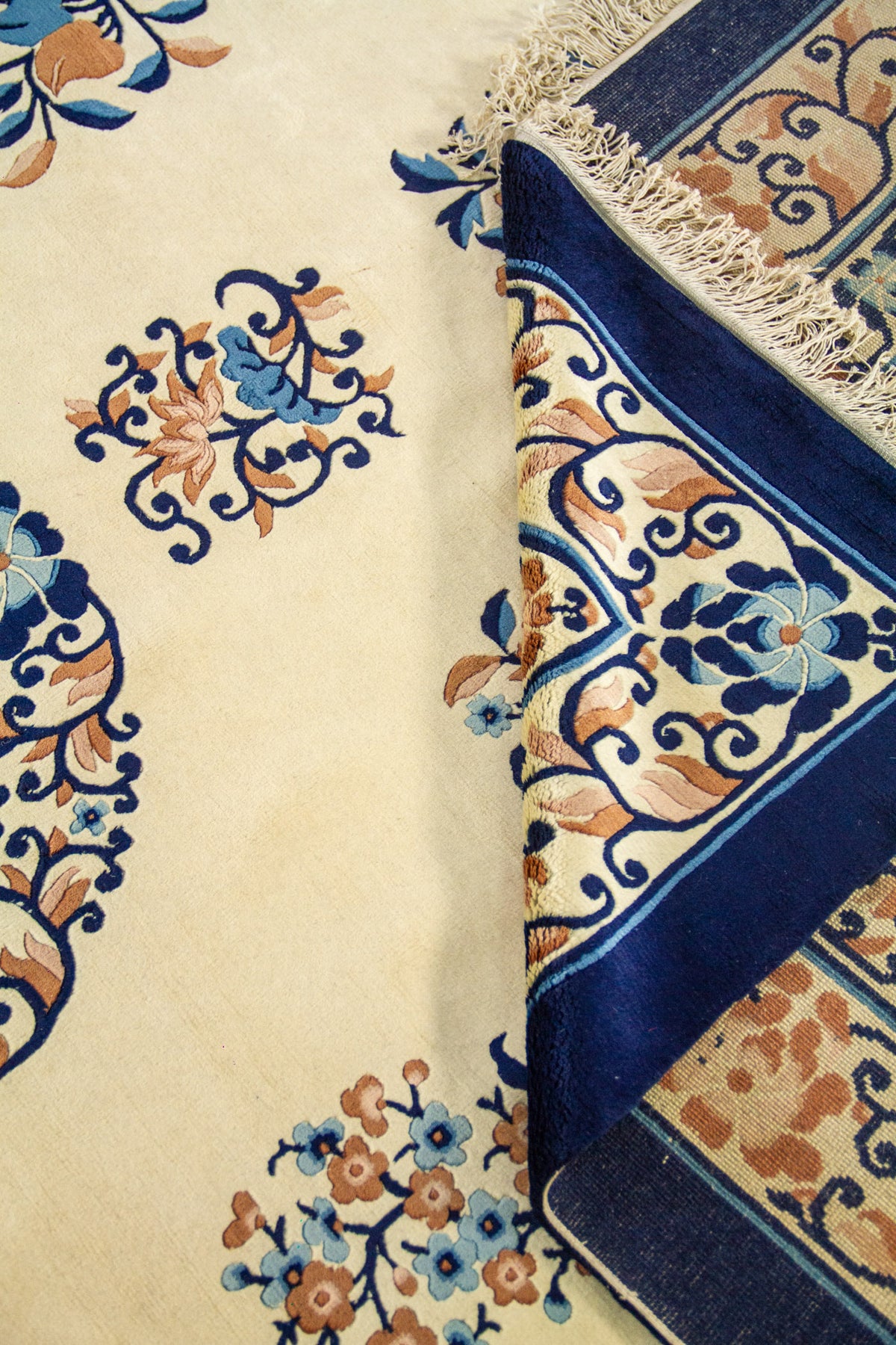 Detalle de la alfombra con pliegue mostrando el grosor y motivos florales pequeños sobre fondo beige.