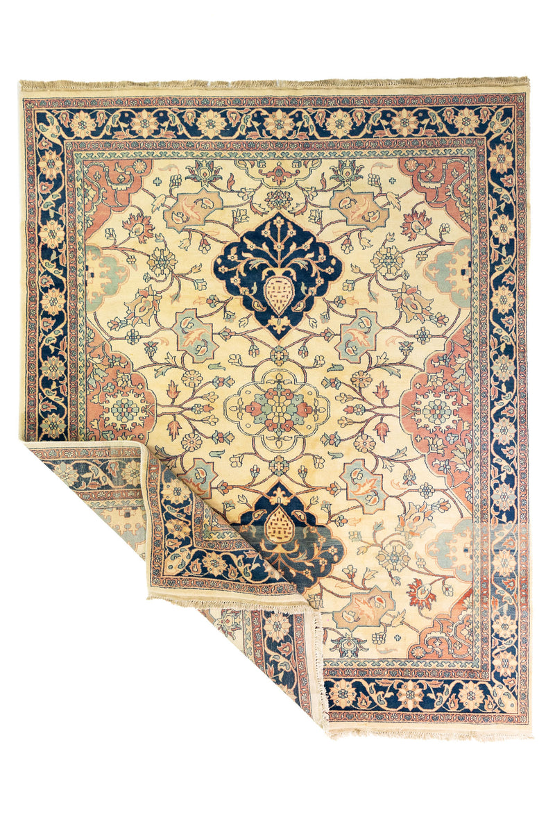 Alfombra Persa Keshan beige y azul de 3.00 x 2.50 mts, vista completa con una esquina doblada; se observan motivos florales, arabescos y medallones de contraste