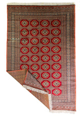 Alfombra Persa Bukara Yamouth rojo de 3.00 x 2.00 mts, vista completa con una esquina doblada; se observan medallones geométricos repetidos y guardas ornamentales