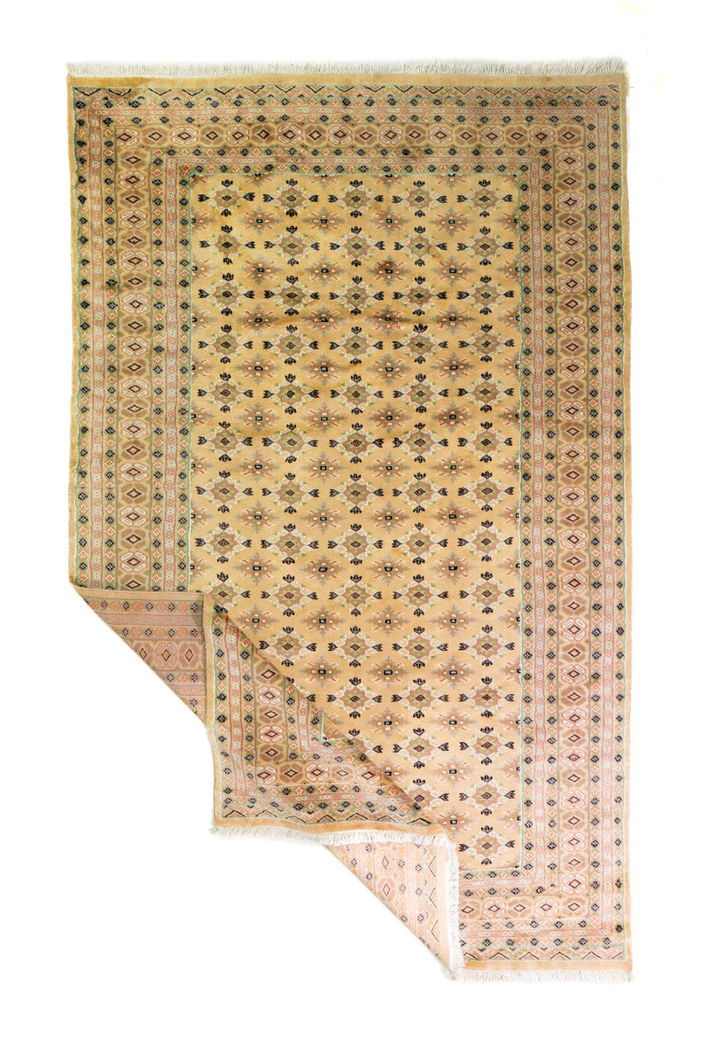 Alfombra Persa Bukara Yamouth beige de 1.83 x 2.90 mts, vista completa con una esquina doblada; se observan pequeños motivos geométricos repetidos y guardas de tono suave