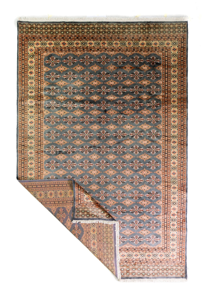Alfombra Persa Bukara Yamouth celeste de 1.88 x 2.85 mts, vista completa con una esquina doblada; se observan motivos pequeños repetidos y guardas geométricas contrastantes
