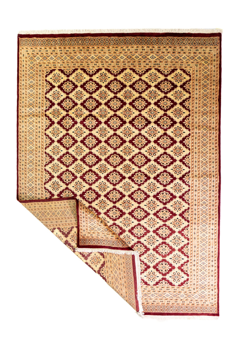 Alfombra Persa Bukara Yamouth beige de 1.88 x 2.60 mts, vista completa con una esquina doblada; se observan entramado geométrico rojizo sobre campo claro