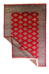 Alfombra Persa Bukara Yamouth rojo de 1.88 x 2.85 mts, vista completa con una esquina doblada; se observan retícula geométrica y guardas claras de contraste