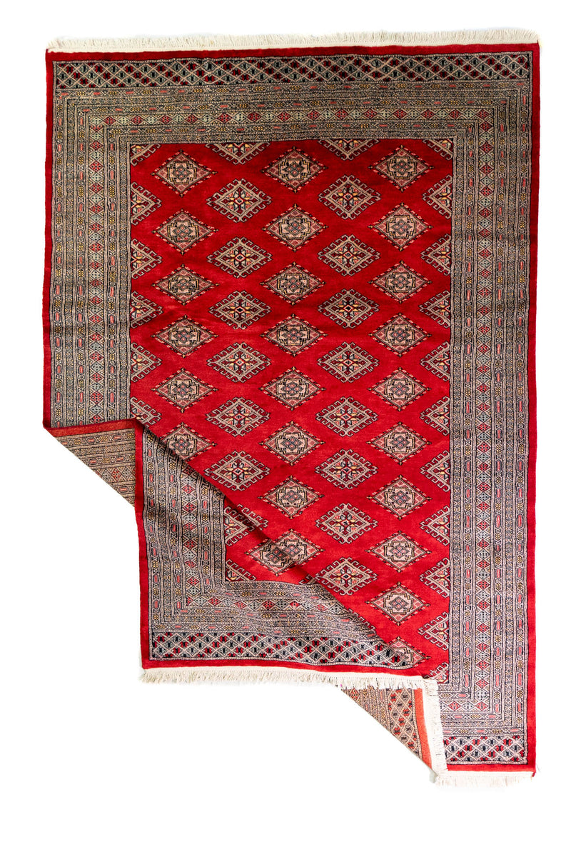 Alfombra Persa Bukara Yamouth rojo de 1.88 x 2.85 mts, vista completa con una esquina doblada; se observan retícula geométrica y guardas claras de contraste