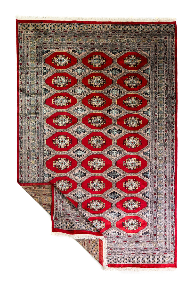Alfombra Persa Bukara Yamouth rojo de 1.90 x 2.90 mts, vista completa con una esquina doblada; se observan medallones ovalados repetidos y guardas de varios niveles