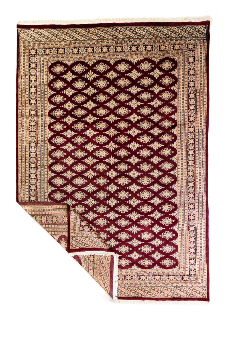 Alfombra Persa Bukara Yamouth bordó de 1.88 x 2.75 mts, vista completa con una esquina doblada; se observan entramado geométrico oscuro y guardas claras