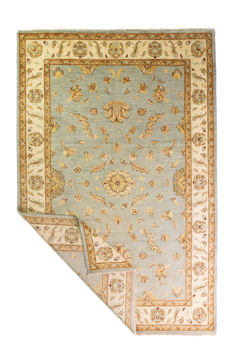 Alfombra Persa Isfahan celeste de 1.85 x 2.82 mts, vista completa con una esquina doblada; se observan motivos florales y vegetales de tono suave con guardas claras