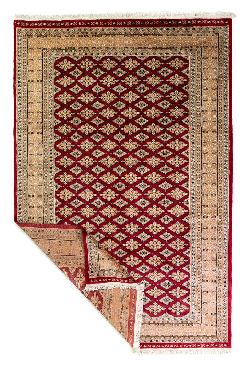 Alfombra Persa Yamouth rojo de 1.83 x 2.87 mts, vista completa con una esquina doblada; se observan retícula geométrica sobre campo intenso y guarda clara