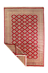 Alfombra Persa Yamouth rojo de 1.75 x 2.52 mts, vista completa con una esquina doblada, mostrando el reverso y la guarda; se observan patrón geométrico de motivos repetidos y bordes contrastantes