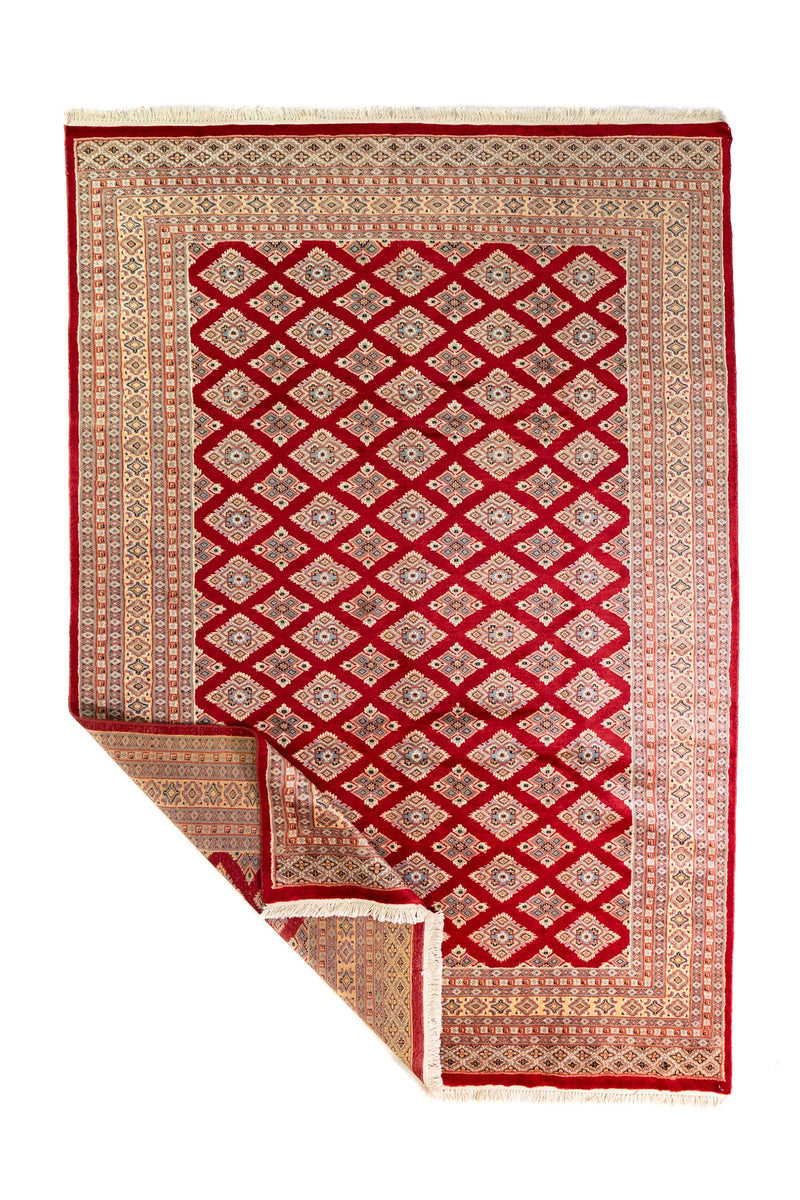Alfombra Persa Yamouth rojo de 1.75 x 2.52 mts, vista completa con una esquina doblada, mostrando el reverso y la guarda; se observan patrón geométrico de motivos repetidos y bordes contrastantes