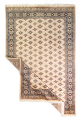 Alfombra Persa Yamouth beige de 1.55 x 2.44 mts, vista completa con una esquina doblada; se observan pequeños motivos geométricos repetidos y guardas sobrias