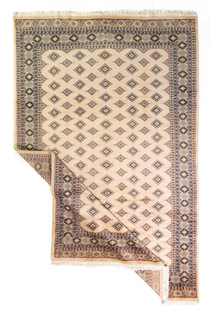 Alfombra Persa Yamouth beige de 1.55 x 2.44 mts, vista completa con una esquina doblada; se observan pequeños motivos geométricos repetidos y guardas sobrias