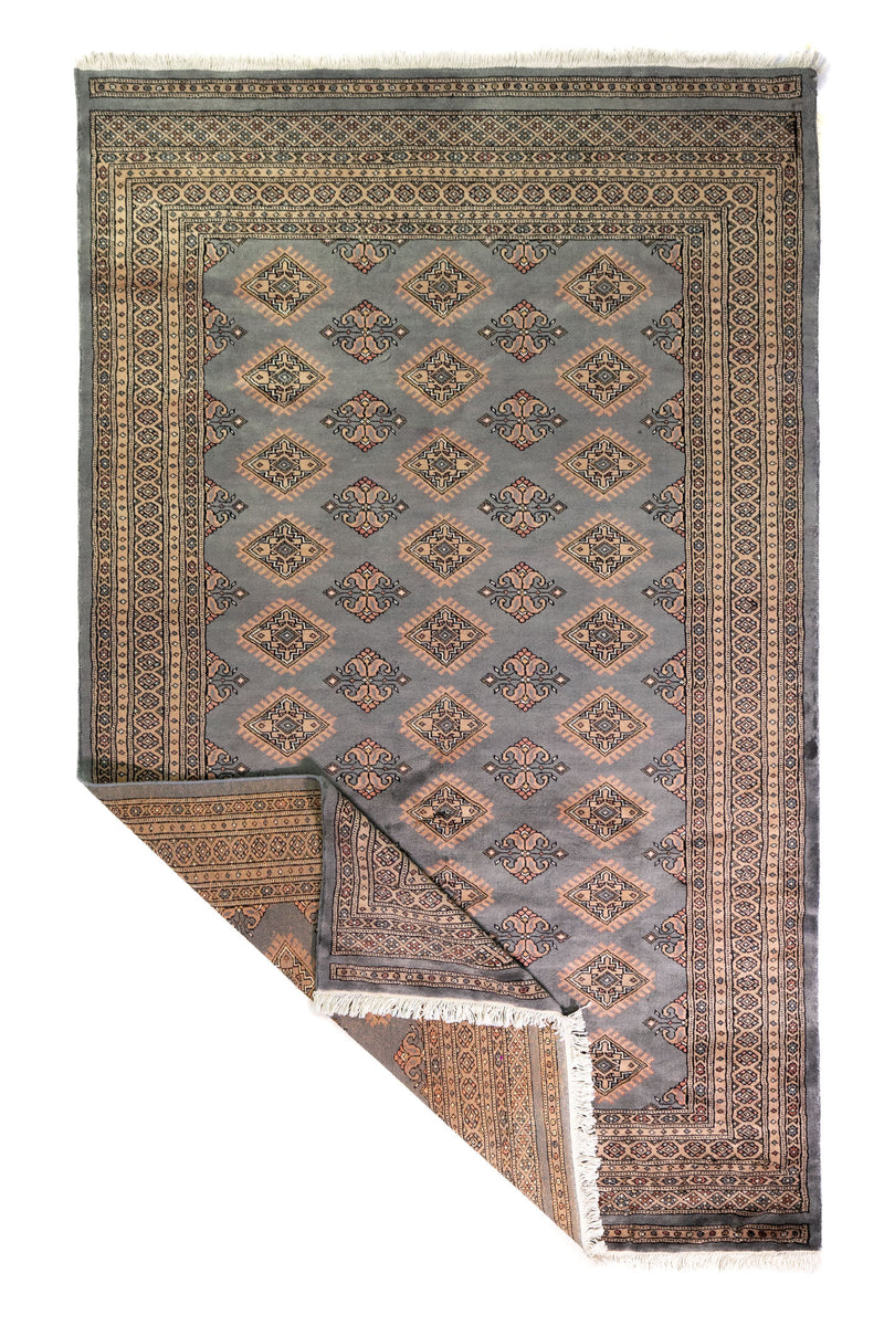 Alfombra Persa Yamouth celeste de 1.55 x 2.48 mts, vista completa con una esquina doblada; se observan rombos repetidos y guardas geométricas