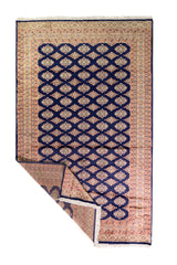 Alfombra Persa Yamouth azul de 1.55 x 2.54 mts, vista completa con una esquina doblada; se observan retícula geométrica azul sobre campo claro