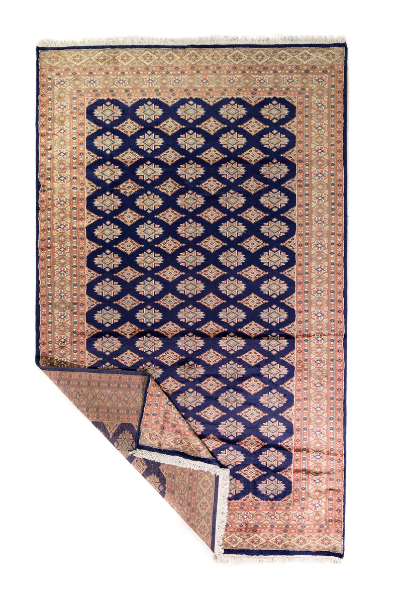 Alfombra Persa Yamouth azul de 1.55 x 2.54 mts, vista completa con una esquina doblada; se observan retícula geométrica azul sobre campo claro