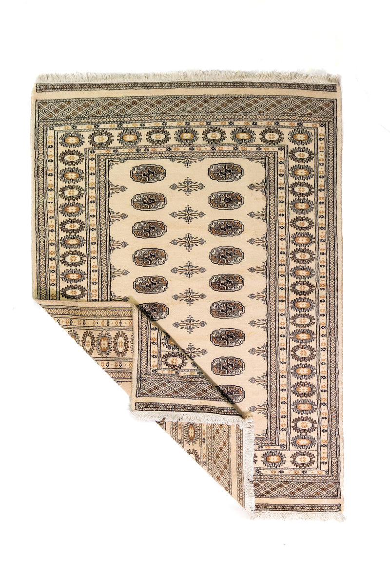 Alfombra Persa Bukara Yamouth beige de 1.24 x 1.73 mts, vista completa con una esquina doblada; el diseño muestra medallones ovalados oscuros alineados sobre un campo claro y guardas geométricas profundas