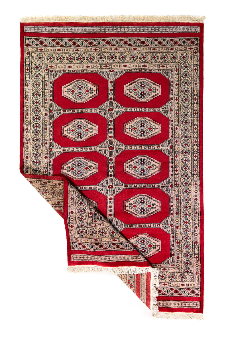 Alfombra Persa Yamouth rojo de 1.25 x 1.90 mts, vista completa con una esquina doblada; el diseño muestra dos columnas de medallones claros sobre un campo rojo y un borde geométrico oscuro