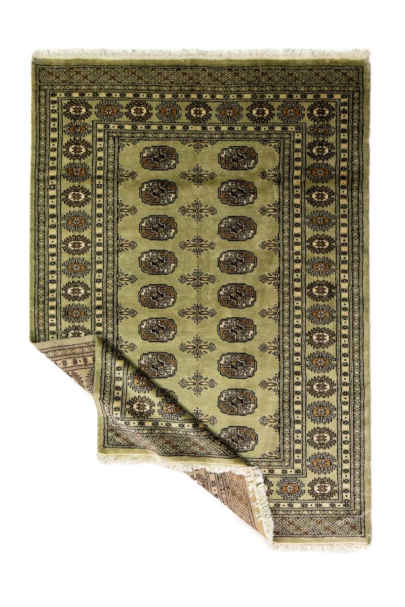 Alfombra Persa Bukara Yamouth verde de 1.24 x 1.78 mts, vista completa con una esquina doblada; el diseño muestra medallones ovalados repetidos sobre un campo verdoso y guardas geométricas oscuras