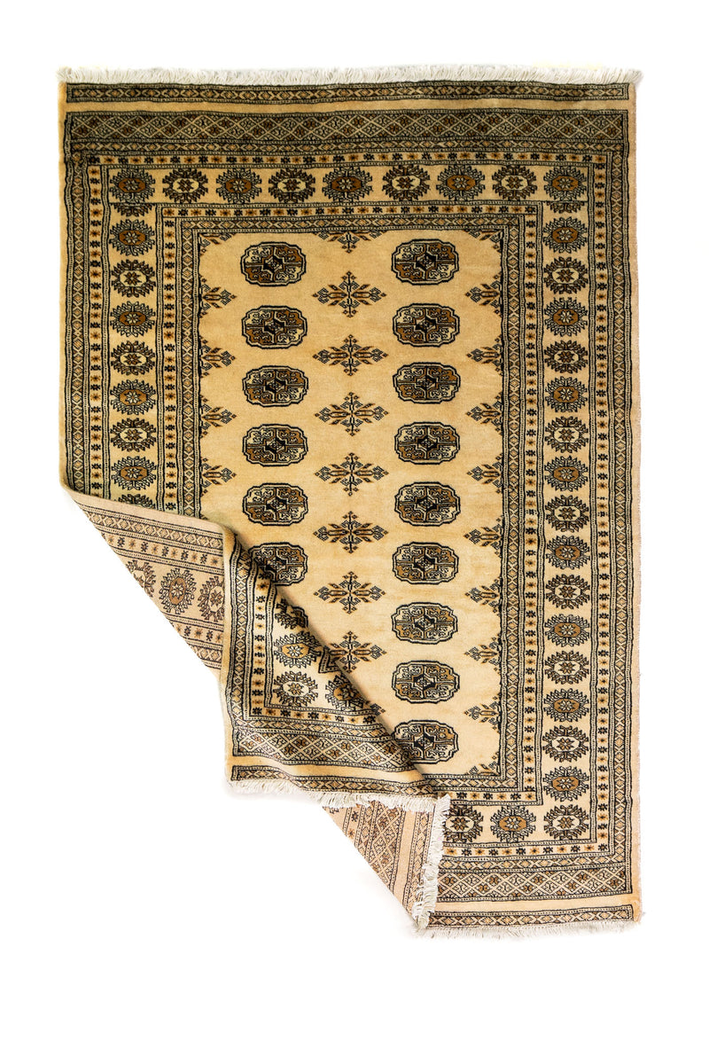 Alfombra Persa Bukara Yamouth beige de 1.24 x 1.93 mts, vista completa con una esquina doblada; el diseño muestra medallones ovalados oscuros sobre un campo beige y un marco de guardas geométricas