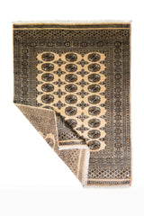 Alfombra Persa Bukara Yamouth beige de 1.27 x 1.80 mts, vista completa con una esquina doblada; el diseño muestra una secuencia ordenada de medallones oscuros sobre fondo beige con borde profundo