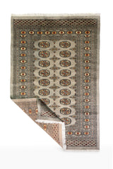 Alfombra Persa Bukara Yamouth celeste de 1.25 x 1.90 mts, vista completa con una esquina doblada; el diseño muestra medallones ovalados y pequeños acentos geométricos sobre un campo celeste grisáceo